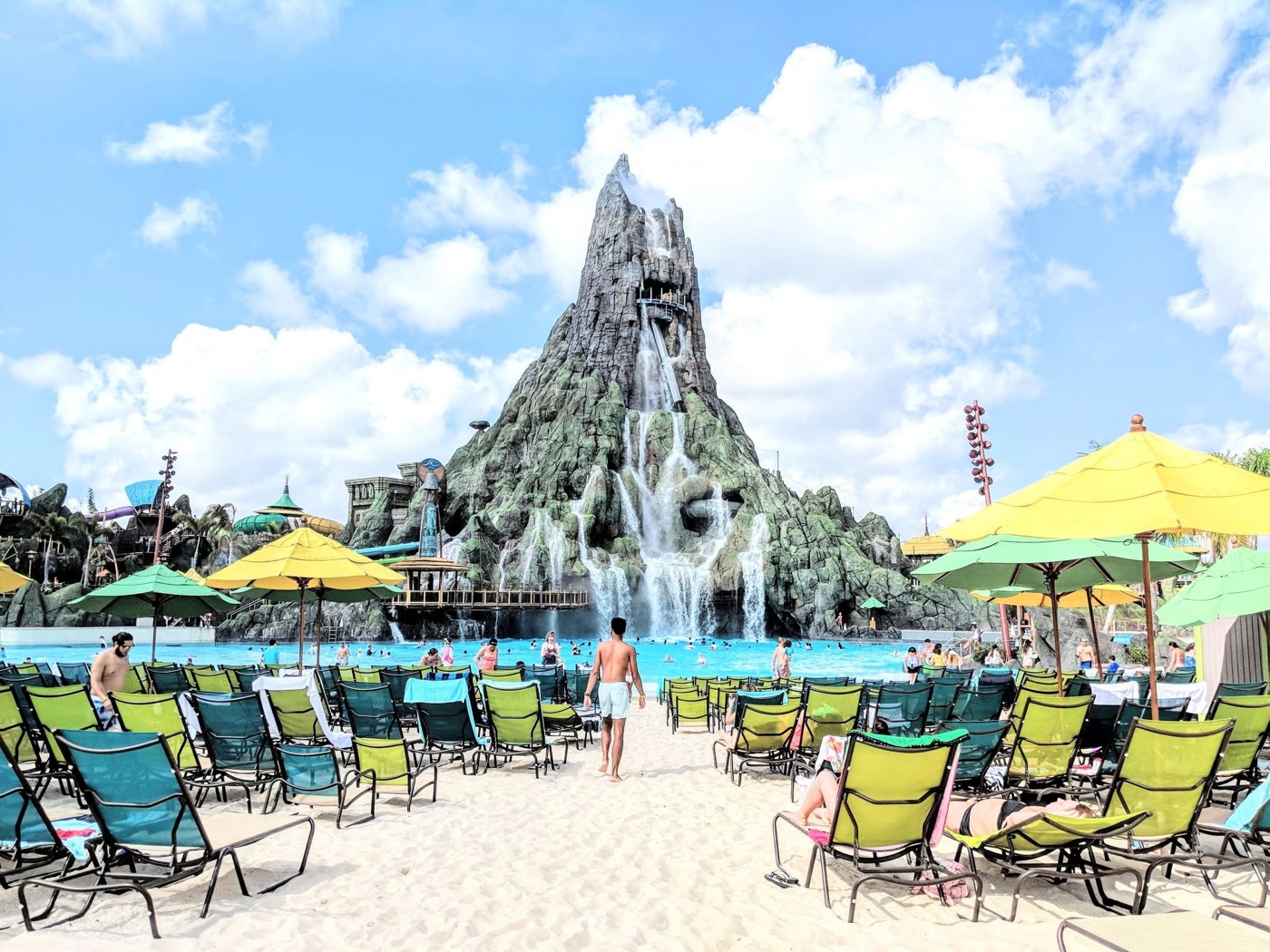 A tropical pool and sandy loungers beneath the Volcano Bay volcano.